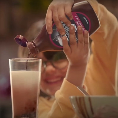 Boy pouring HERSHEY'S SYRUP in a glass of milk